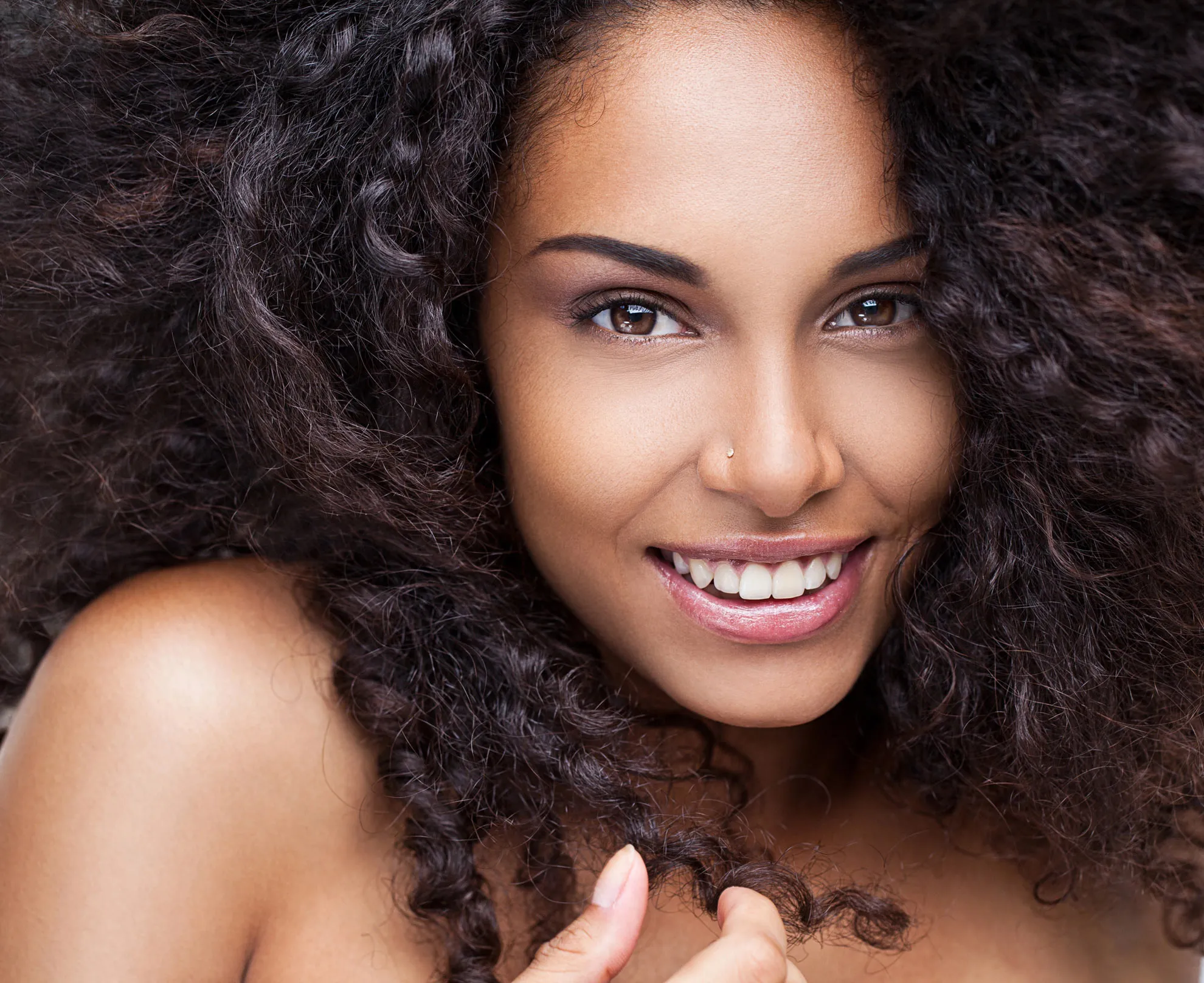 Smiling woman with curly hair and nose stud.